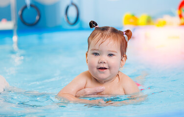 Fototapeta na wymiar Happy little baby girl swims in pool with trainer, concept development of muscles body and health care of kid