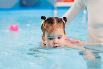 Happy little baby girl swims in pool with trainer, concept development of muscles body and health care of kid