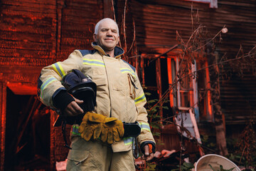 Fototapeta na wymiar Portrait happy Officer fireman in uniform with helmet near wooden house after burning. Concept rescue service after successful call
