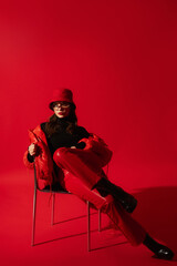 Fashionable confident woman wearing trendy oversized red puffer down jacket, sunglasses, bucket...