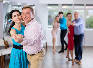 Portrait of positive adult pairs of different ages enjoying tango in modern dance hall together