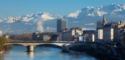 Cityscape of Grenoble with famous cable car against backdrop of snowy Alps in sunny day, France - obrazy, fototapety, plakaty