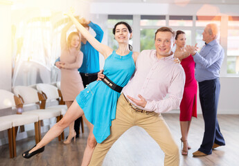 Fototapeta premium Positive men and woman dancing slow ballroom dance during group class in choreography studio
