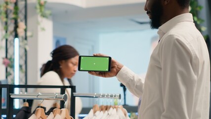 African american shopper holding green screen smartphone in cheap thrift shop with vintage clothes....