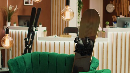 Skies and snowboard in lounge area at hotel ski resort during winter season, empty reception used for wintertime leisure activities. Alpine sport equipment with helmet and goggles.