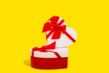 A stacked arrangement of two heart shaped gift boxes with vibrant red ribbons on a yellow background