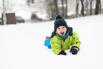 Fototapeta na wymiar Portrait of Little Happy Boy Lies in Snow
