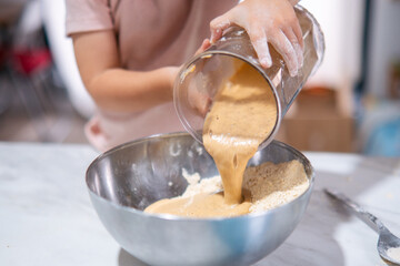 Niña pequeña añadiendo alimento batido en un bol cromado.