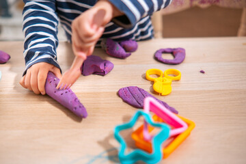 Manos de niña de  2 años jugando con plastilina casera y moldes. Jugar con la plastifica en casa, juguetes educativos para niños Montessori. Juegos creativos para niños pequeños. 