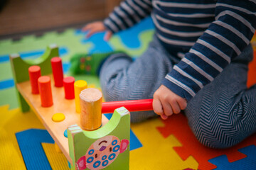 Bebé entretenido con juego sensorial en el suelo. Juguete Montessori educativo, martillo de madera. - obrazy, fototapety, plakaty