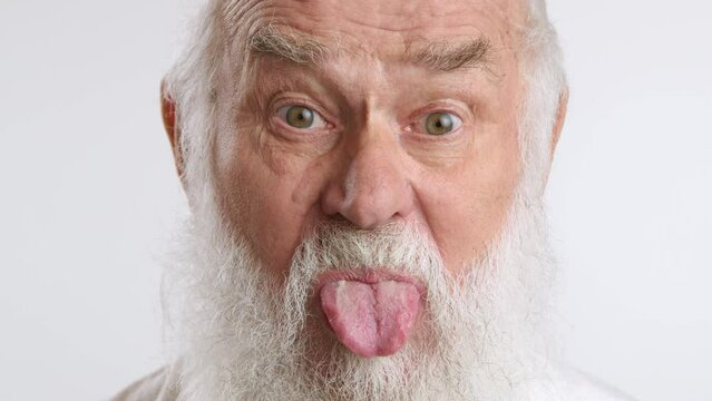 Close-up of a playful elderly man sticking out his tongue in a humorous and lighthearted manner, wearing a denim vest, capturing his jovial and spirited personality. Camera 8K RAW. 