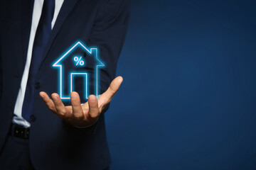 Fototapeta na wymiar Mortgage rate. Man holding illustration of house with percent sign on dark blue background, closeup. Space for text