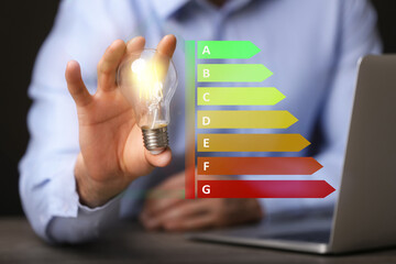 Energy efficiency rating and man holding glowing light bulb at table, closeup
