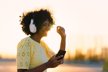 Side view of a cheerful african woman dancing listening to music outdoors during sunset