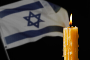 Fototapeta premium Burning candle against flag of Israel on black background