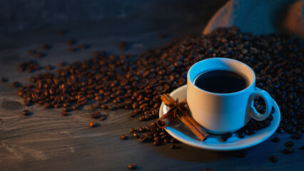 A white cup of black coffee on a wooden table with roasted coffee beans and copy space