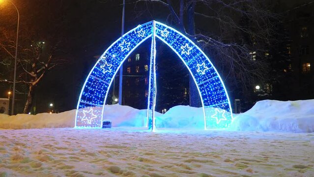 New Year glowing decorative arch with decoration and flashing lights. Blue and white garlands. Holiday decor. Winter evening. Decorative arch against the backdrop of Kuibyshev Street and Lenin Avenue