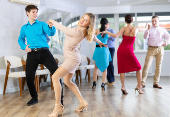 Positive adult woman enjoying active dances with young male partner in modern dance studio,...