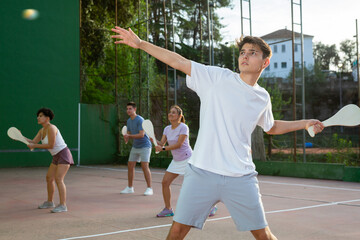 Portrait of sporty young guy playing pelota on open fronton court on summer day, ready to hit...