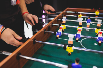 Group of friends playing kicker in a sports bar room, colleagues teammates play table football,...