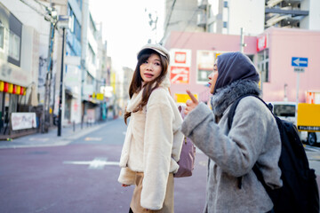 Obraz premium woman girl tourist Two Asian friends but different religions, one of whom is a Muslim girl. Walking tour of the city, city view, traveling in Japan. with fun She is traveling in the city area.