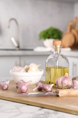 Obraz na płótnie Canvas Fresh raw garlic, knife and oil on white marble table, closeup
