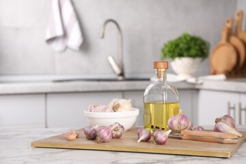 Fototapeta na wymiar Fresh raw garlic, knife and oil on white marble table, space for text