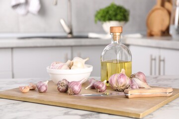 Fototapeta na wymiar Fresh raw garlic, knife and oil on white marble table