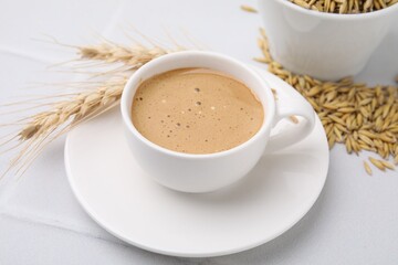 Cup of barley coffee, grains and spikes on white table, closeup