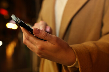Woman using smartphone on blurred background, closeup