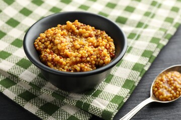 Bowl and spoon with whole grain mustard on black wooden table
