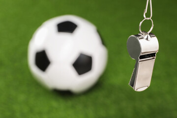 Football referee equipment. Metal whistle and soccer ball on green grass, closeup with space for...