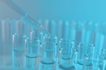 Laboratory analysis. Dripping liquid from pipette into glass test tube on light blue background, closeup