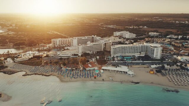 Aerial view of Mediterranean coastline in the sunset. Turquoise crystal water on Nissi Beach, Ayia Napa, Cyprus. Hotels resort complex on the first line. Travel destination landscape. Summer vacation.
