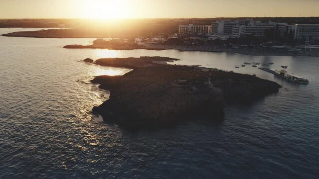 Mediterranean sea coast travel background, sunset landscape. Rocky silhouette island near sea shore of Nissi beach in Cyprus. Beautiful nature landscape. Summer vacation, holiday. Aerial drone flight
