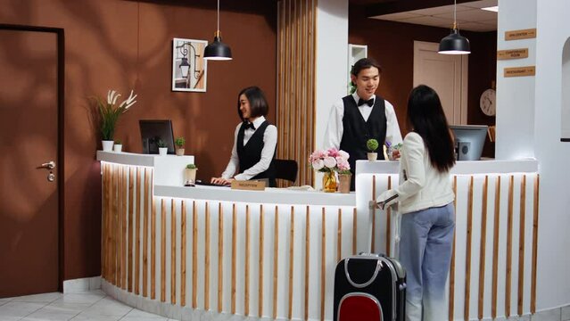 Tourist entering hotel reception to go through registration, confirming booking after long flight. Asian woman on holiday at five star resort, talking to front desk staff about room facilities.