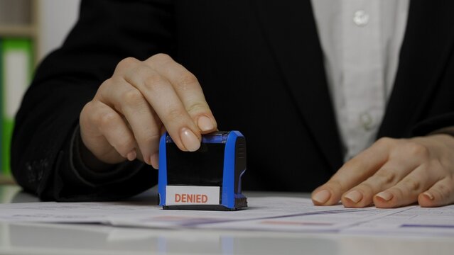 Close up shot of person visa application document. Shot of female worker puts stamp with denied mark written on it.