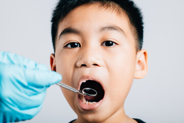 A pediatric dentist examines a child's mouth after extracting a loose milk tooth. Dental tools aid...