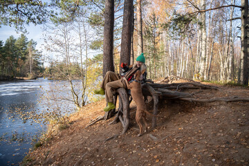 Pet owner sitting on pine tree root while resting after hiking in pine forest, playing with dearest...