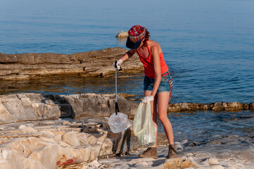 Adult Female Ecologist Volunteer Picking Up Plastic Garbage Trash From a Coastline