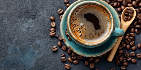 Overhead shot of a cup of coffee on a dark textured surface with coffee beans.