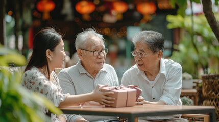 Asian couple surprised elderly father with Birthday gift at outdoor cafe restaurant on summer holiday vacation. Family relationship, celebrating father's day and older people health care concept. - obrazy, fototapety, plakaty