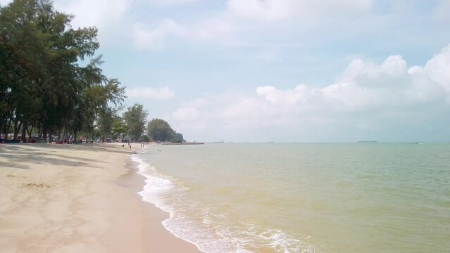 Daytime view of Pantai Puteri Beach in Malacca. Waves from the sea gently dissipate on the shore. The footage starts low and rises like a drone shot.