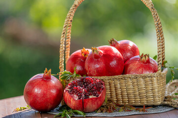 Red Pomegranate in wooden basket on wooden table in garden, Pomegranate with slices on blurred greenery background.
