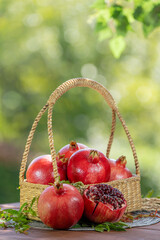 Red Pomegranate in wooden basket on wooden table in garden, Pomegranate with slices on blurred greenery background.