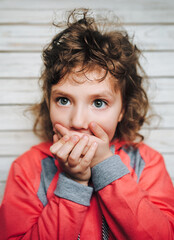 Little girl covering her mouth with her hands. Surprised or scared. On the light background...