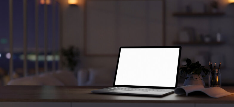 Dark workspace close-up image with a white-screen laptop computer on a desk in a modern living room.