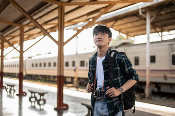 A handsome, happy young Asian man tourist backpacker standing at a platform in a railway station.