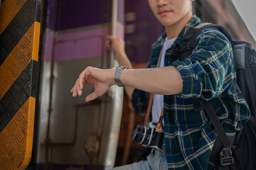 A handsome Asian man traveler is checking time on his wristwatch while getting off the train.