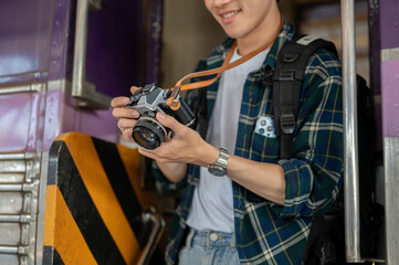 An Asian man traveler backpacker is taking pictures with his camera while getting off the train.